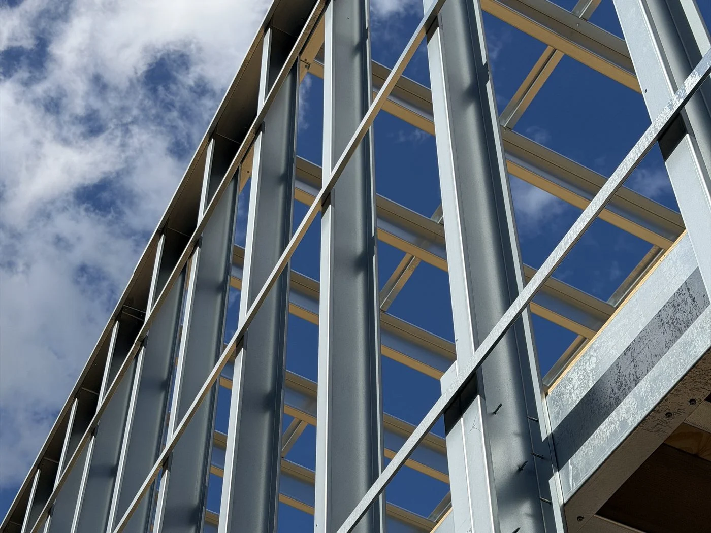 Our SFS wall frame on site: galvanised studs and rails spanning the floors, seen from below against the sky
