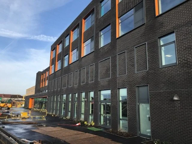 Long dark brick-slip elevation with orange window surrounds, new paving in front.