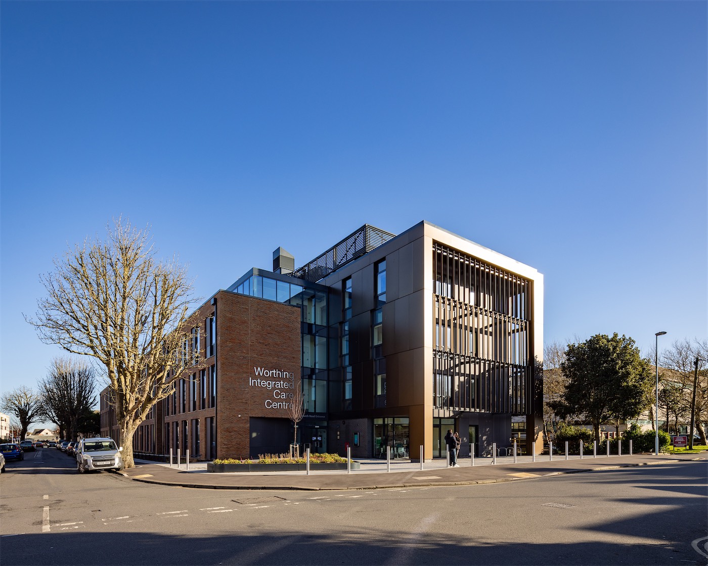 Worthing Integrated Care Centre on its street corner: bronze aluminium fins and rainscreen panels under a blue sky
